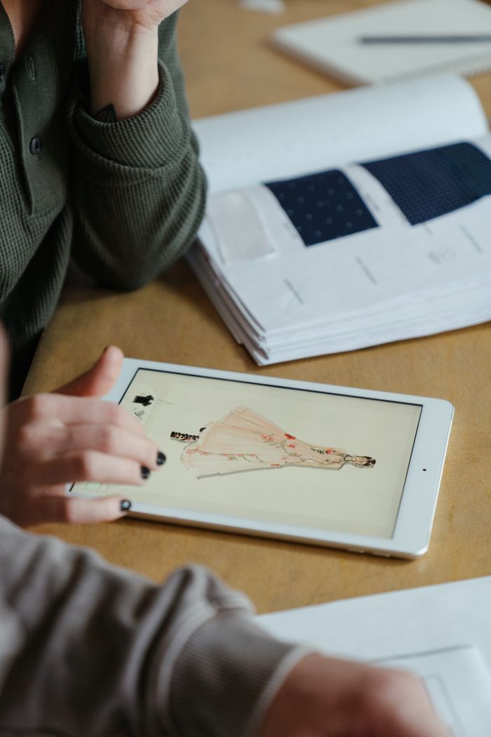 Close-up of fashion designer sketching clothing designs on a tablet at a workshop table.