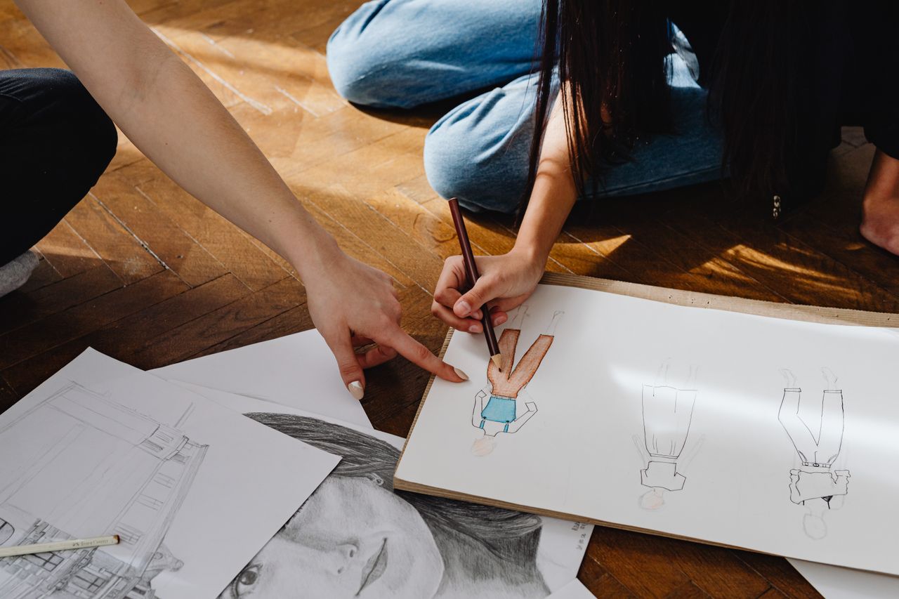 Close-up of hands sketching fashion designs on paper indoors.