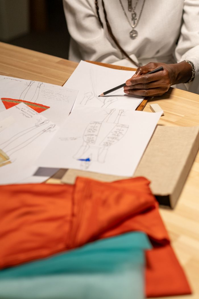 Fashion designer sketching new clothing designs with fabric samples on a desk.